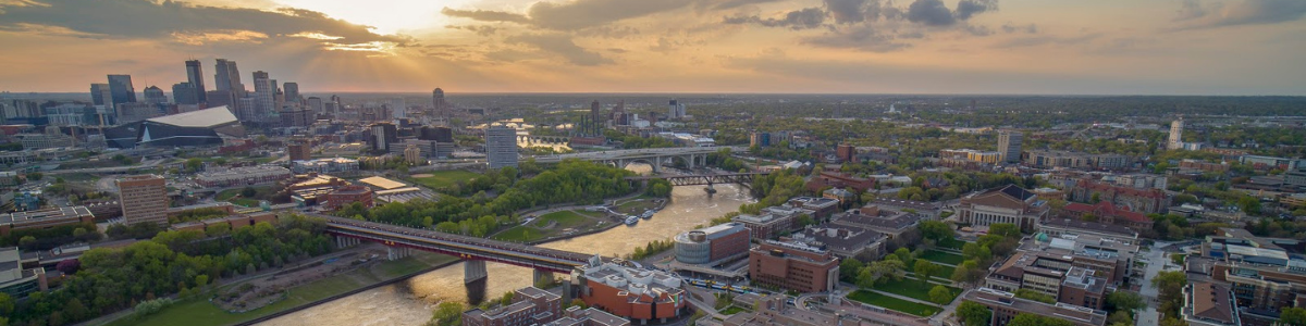 A sunset with a city skyline below and an aerial view of UMNTC Minneapolis campus